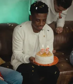 Man holding a birthday cake with lit candles as confetti falls at a party